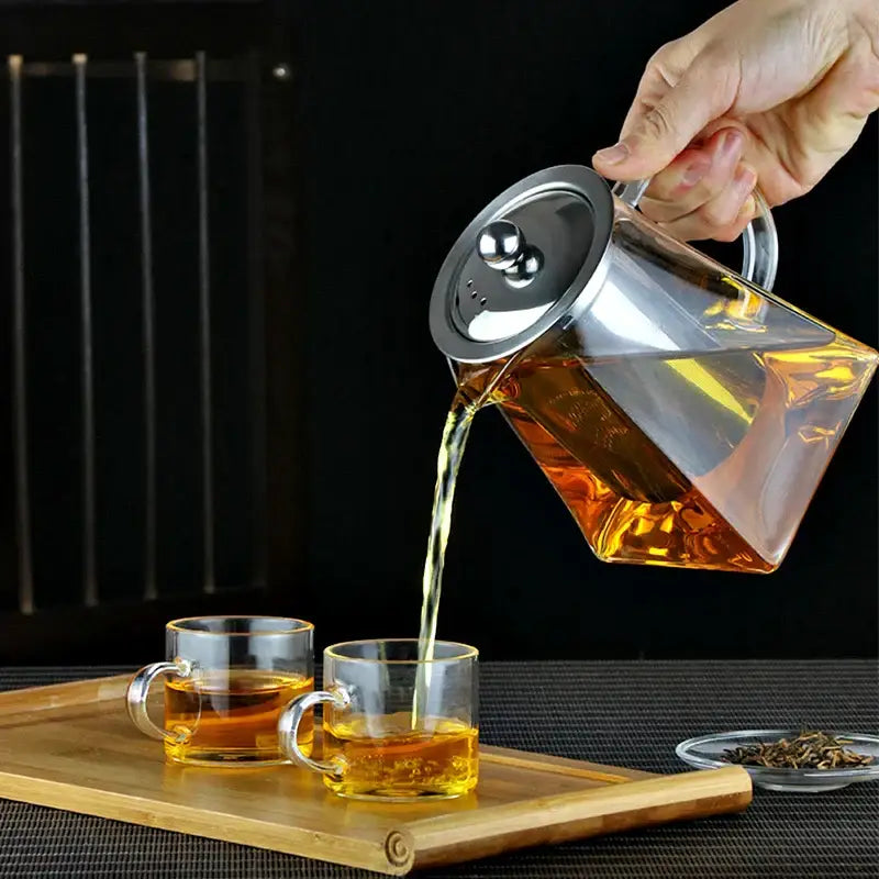 Clear glass decorbites™ teapot with stainless steel infuser pouring amber tea into matching clear glass cups