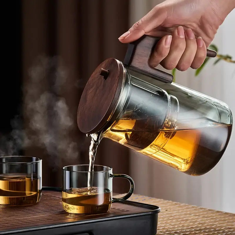 Decorbites glass teapot with dark wood handle and lid filled with steaming golden tea with one-button filtering