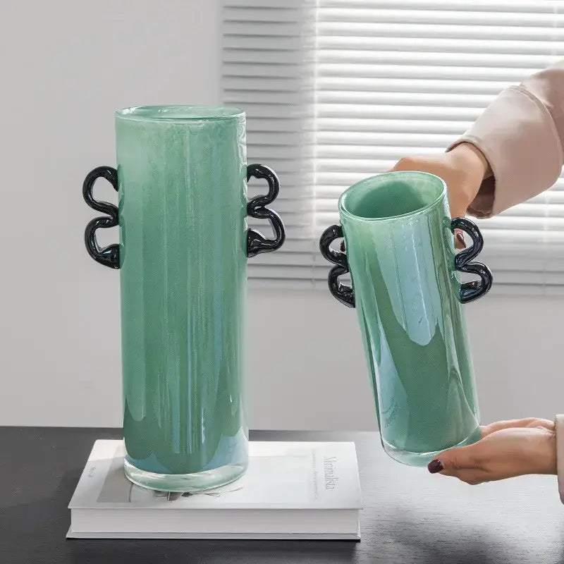 A translucent mint-green decorbites glass vase with sleek black twisted handles for flower arrangement and home decoration