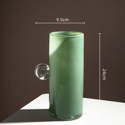 A translucent sage green decorbites glass vase with a clear geometric sphere handle for flowers and accessories