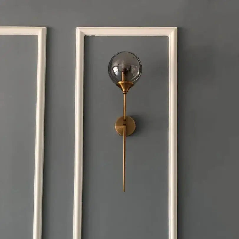 A sleek brass DecorBites glass wall lamp with smoked glass globe and slender stem for bedroom lighting