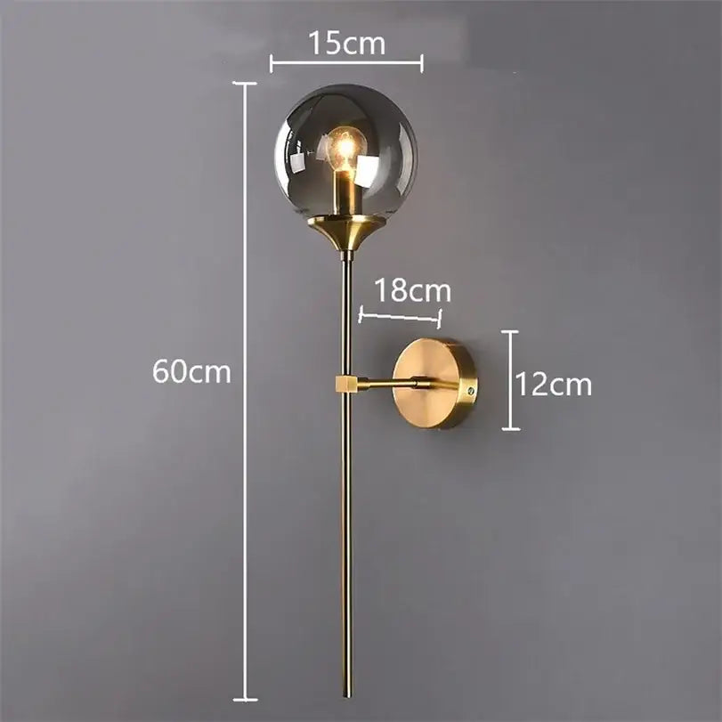 Modern brass-finished decorbites glass wall lamp with spherical smoked glass globe and slender stem for bedroom lighting