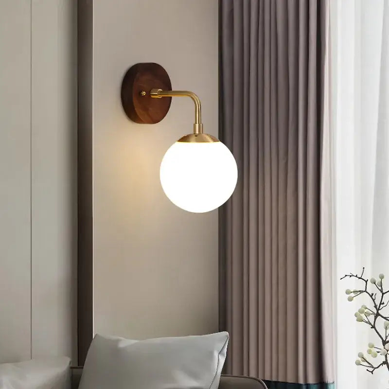 A sleek brass-finished decorbites glass wall light fixture with round frosted globe and walnut wood backplate