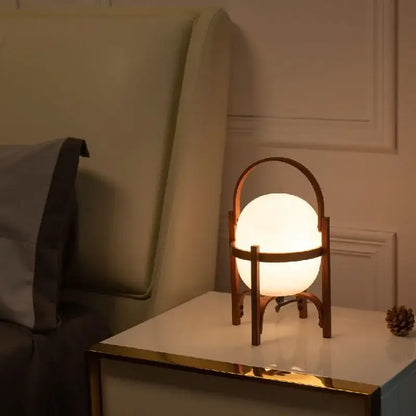 Warmly glowing DecorBites glass and wood metal table lamp with opaque white globe and minimalist wooden frame handle