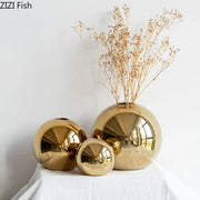 Set of three glossy golden ball ceramic vases with reflective surfaces arranged on white surface for home decor