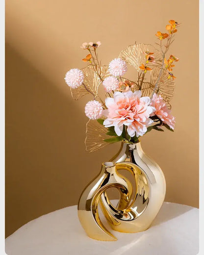 DecorBites™ golden flower vase is a sleek gold-toned ceramic vase with intertwined swirl design holding pink flowers