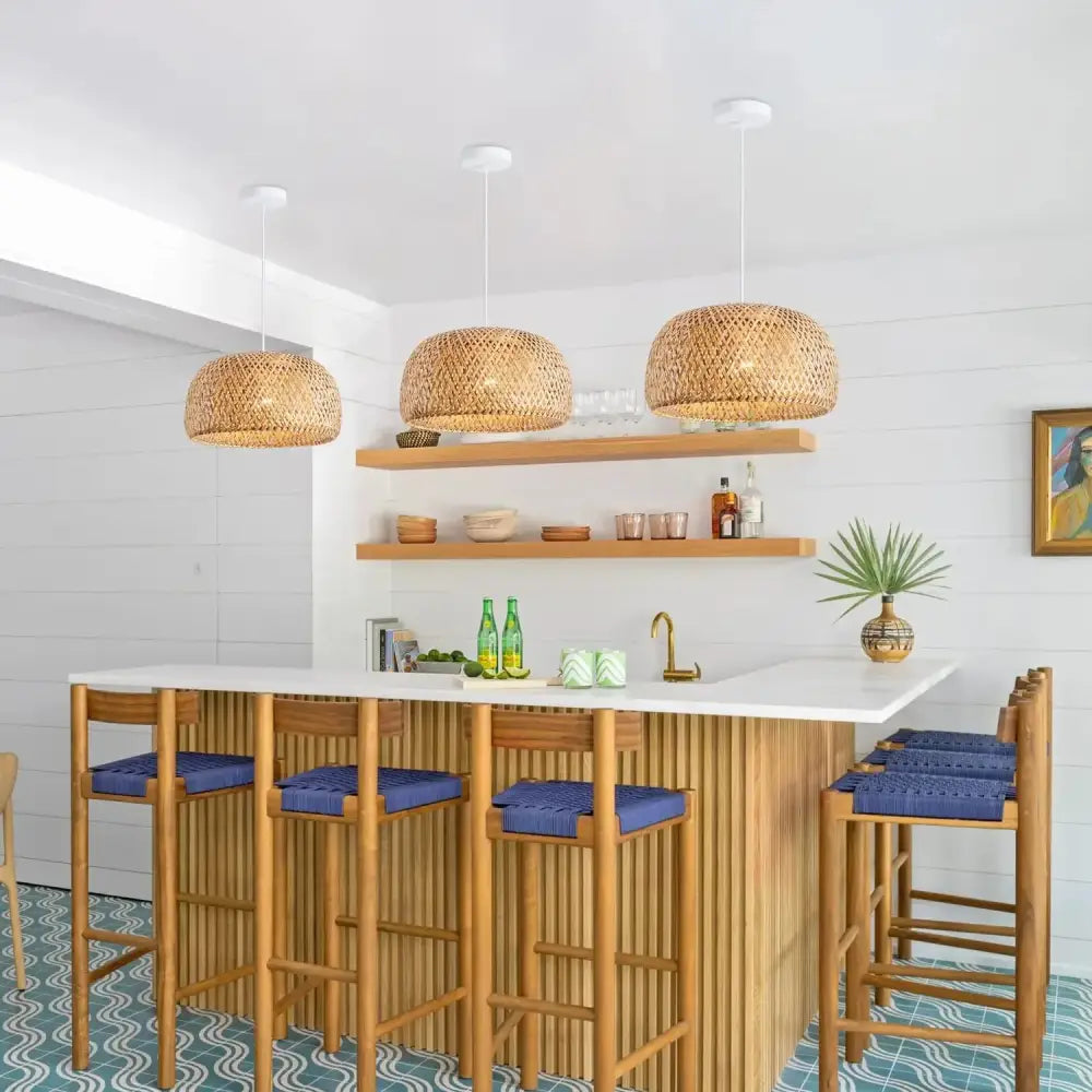 Three hand-woven bamboo lantern pendant lights hang above a wooden bar with blue cushioned stools for decorbites