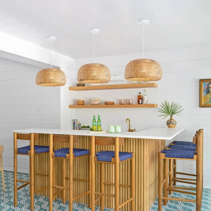 Three hand-woven bamboo lantern pendant lights hang above a wooden bar with blue cushioned stools for decorbites