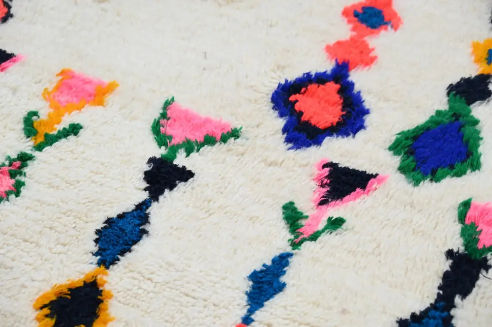 A handmade moroccan azilal carpet featuring a fluffy white base with vibrant abstract floral patterns in pink blue green and black
