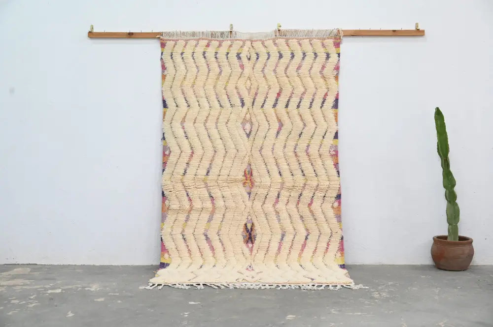 Cream-colored handmade moroccan azilal rug with bold zigzag pattern in muted purples oranges yellows and fringed edges