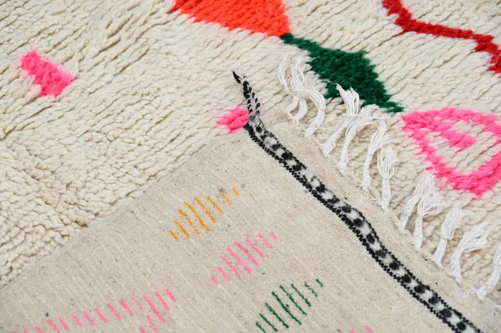 Cream-colored moroccan handmade azilal rug with vibrant pink green and orange geometric patterns in natural wool