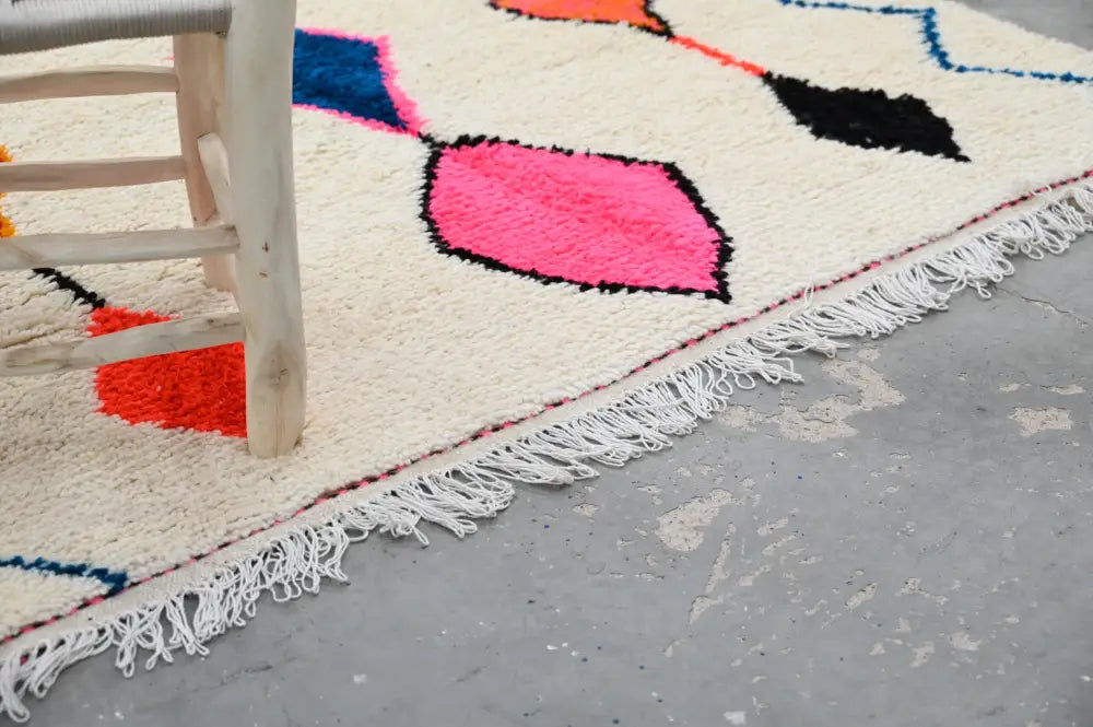 Cream-colored handmade moroccan azilal rug with vibrant colors and bold geometric patterns featuring fringed edges