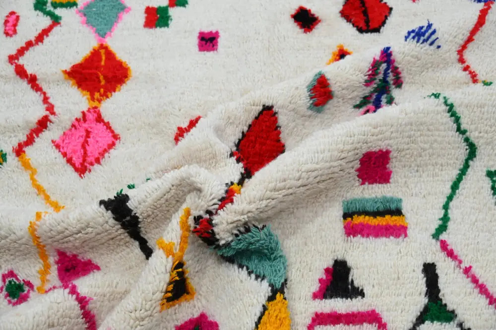 A plush off-white handmade traditional azilal rug with vibrant red pink teal green yellow and black geometric patterns