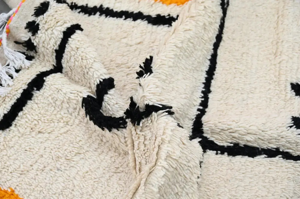 Cream-colored plush wool moroccan azilal rug with bold black geometric patterns and orange accents 240x152 cm
