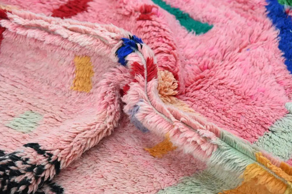 A plush handmade Moroccan Azilal rug with vibrant pink base and bold geometric patterns in multiple colors