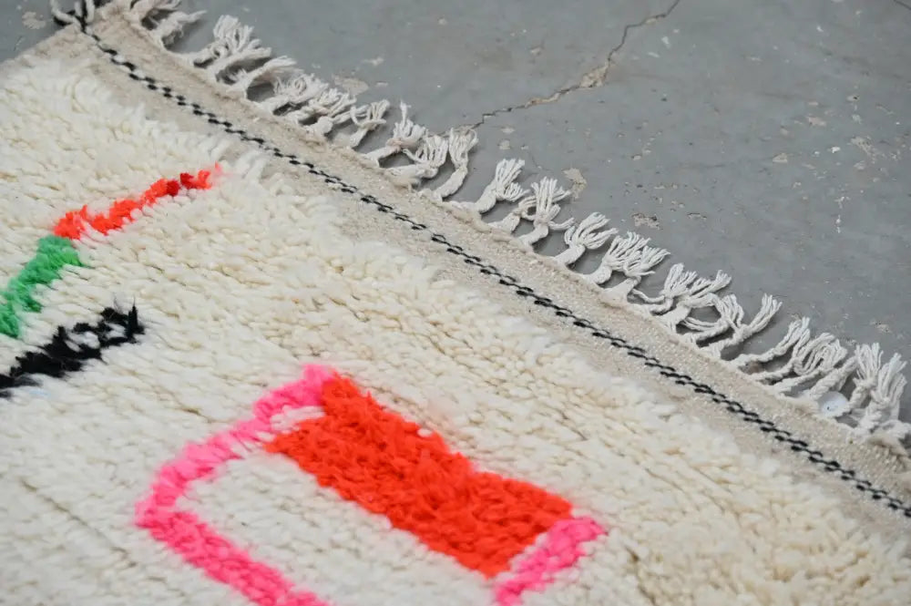 Cream-colored handmade moroccan azilal rug with vibrant geometric patterns and fringed edges by decorbites