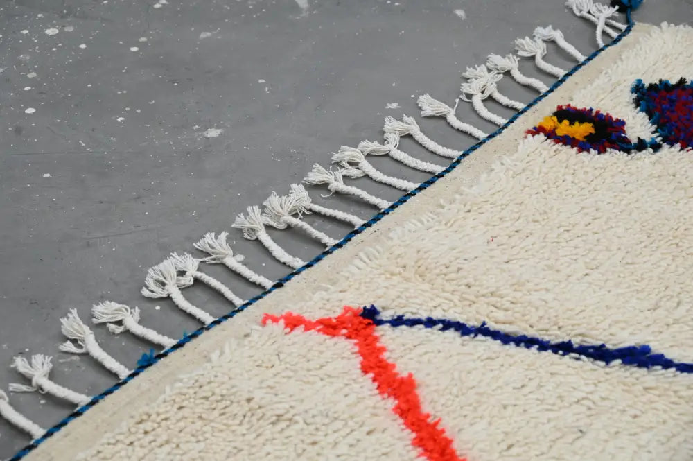 Cream-colored handmade traditional azilal rug with white fringe and red and blue geometric patterns 250x145 cm
