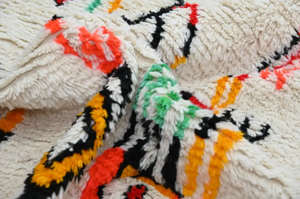 A plush cream-colored decorbites™ handmade moroccan azilal rug with bold geometric patterns in black orange red and green