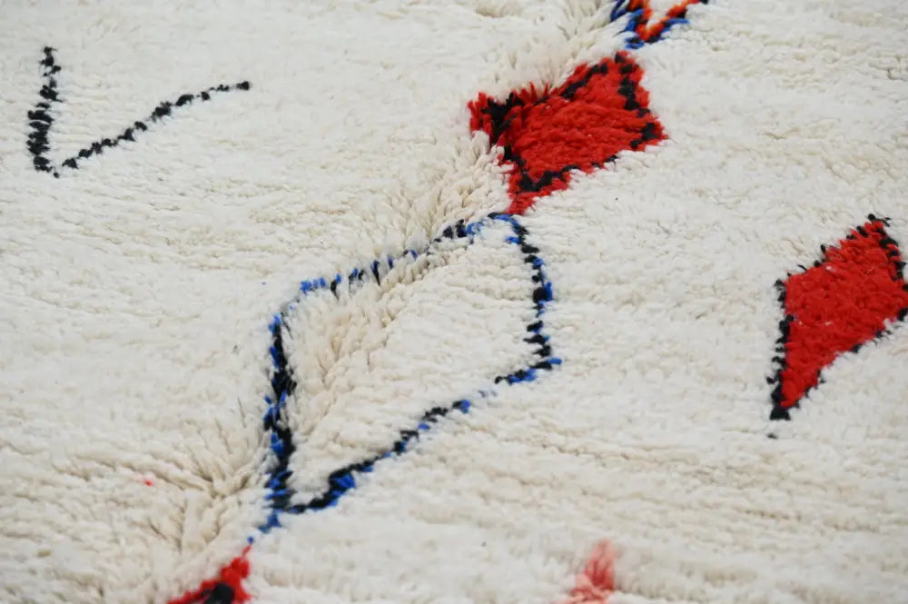 Creamb-colored handmade moroccan azilal rug with bold red and navy blue geometric patterns in thick wool texture