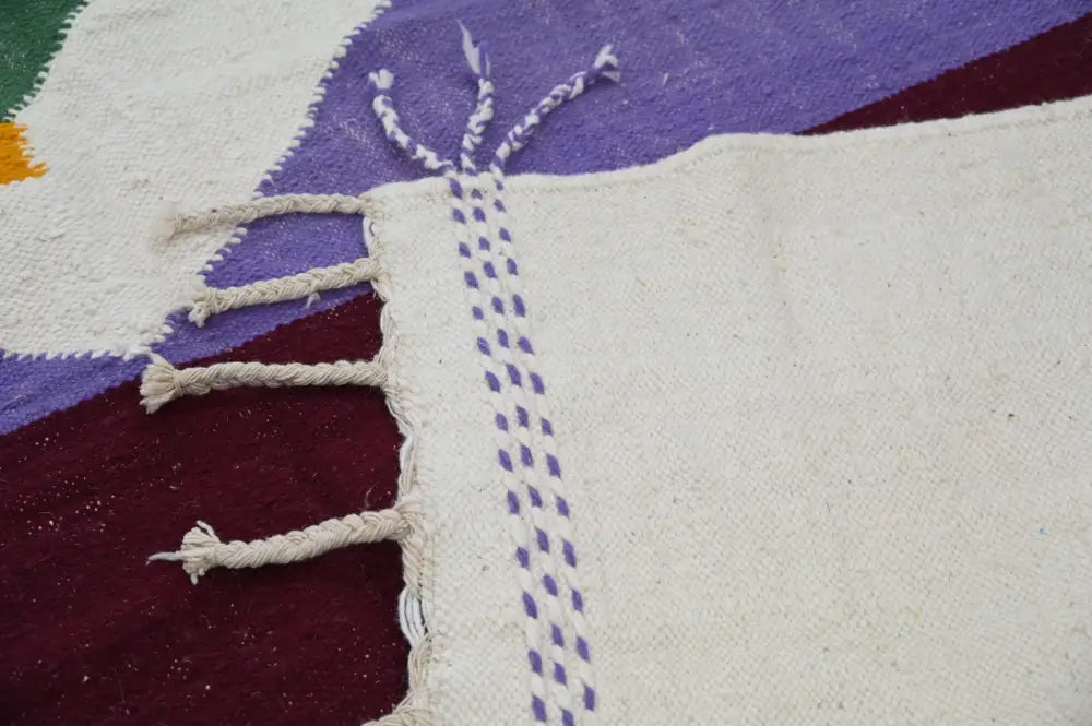 Cream-colored moroccan handmade azilal rug with purple and maroon geometric patterns and white braided fringe