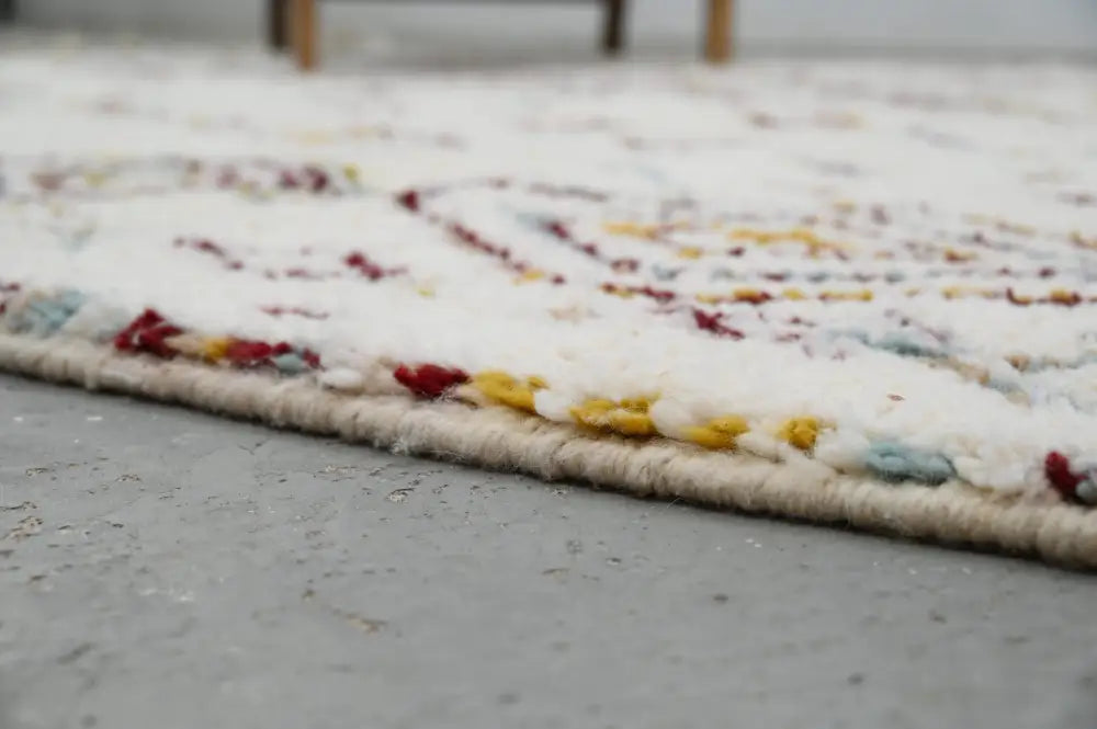 A soft white handmade moroccan azilal rug with a colorful geometric pattern along the edge 305x206cm
