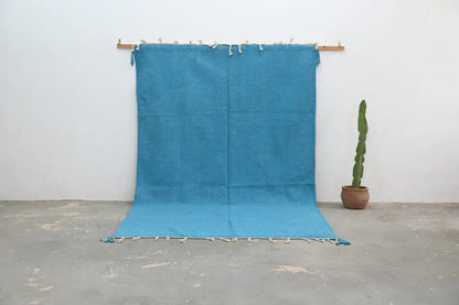 A vibrant turquoise handmade azilal rug 306x200cm with fringed edges and tassels displayed on a wooden rod