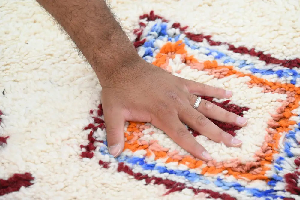 A hand with a silver ring rests on a colorful handmade moroccan azilal rug with bold red orange and blue patterns