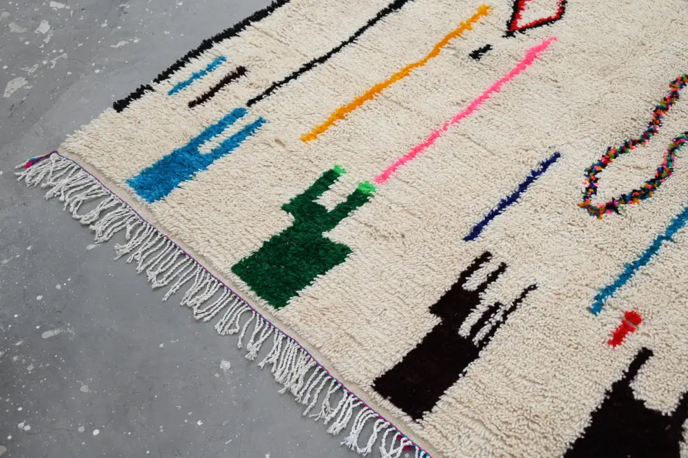 Cream-colored moroccan azilal rug with bold black blue green orange pink red geometric patterns and fringed edge 313x194cm