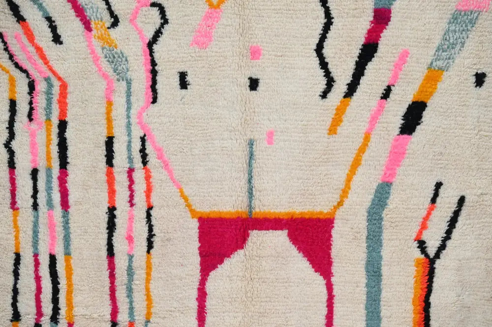 A cream-colored handmade moroccan azilal rug with bold abstract geometric patterns in pink, magenta, black, orange, and teal