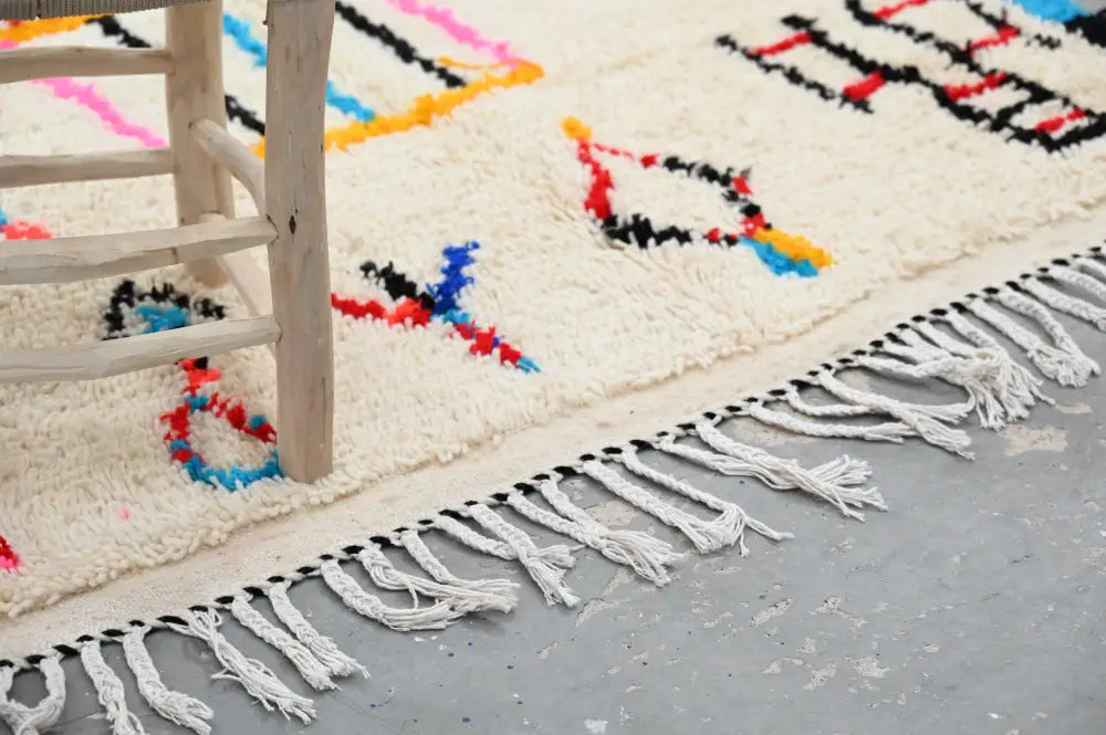 Cream-colored handwoven moroccan azilal rug with bold red blue black yellow geometric patterns and long white fringe edge