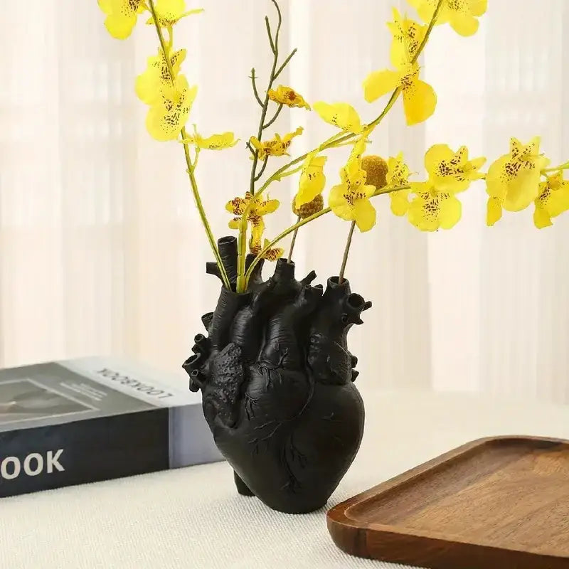 Black anatomically detailed heart shape resin vase by DecorBites holding yellow orchids in a decorative display