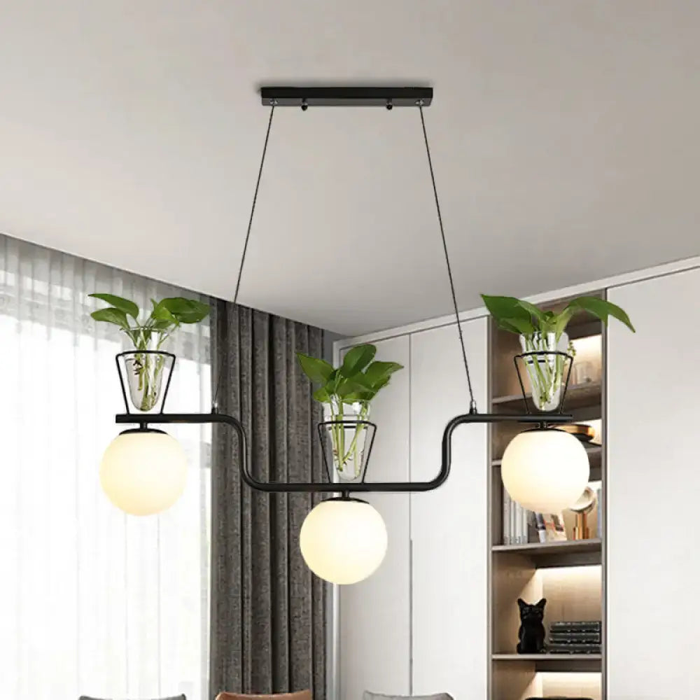 Modern black metal pendant light with three opal glass globes and clear glass pots holding green plants by DecorBites™