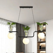 Modern black metal pendant light with three opal glass globes and clear glass pots holding green plants by DecorBites™