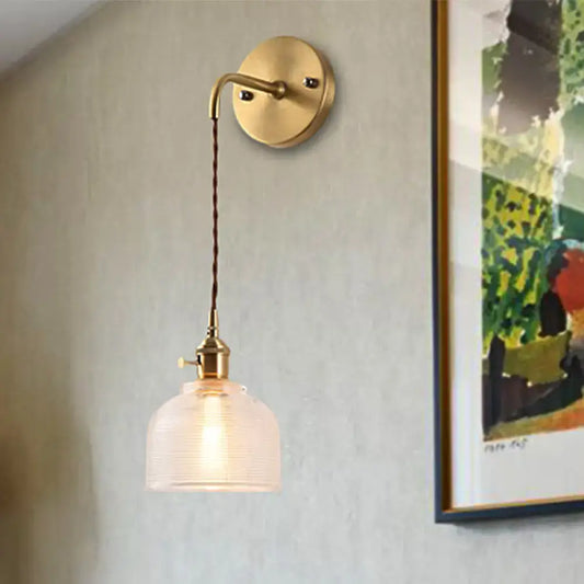 Industrial brass sconce featuring a brass finish with a textured glass dome and twisted cord for bedroom lighting