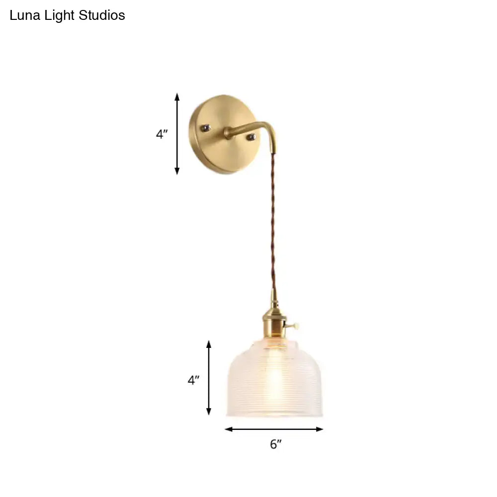 Industrial brass sconce featuring a textured glass dome with frosted finish and twisted cord for bedroom lighting