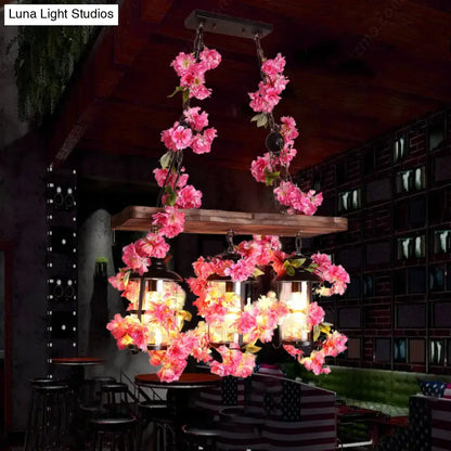 A rustic wooden chandelier with vibrant pink flowers and clear glass hanging lanterns as a restaurant island light with three cylindrical heads