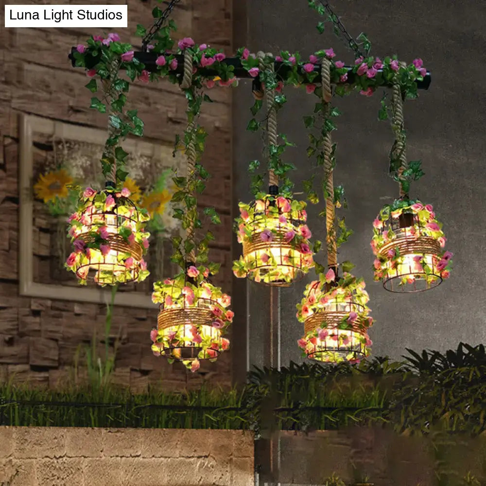 Three hanging black cage island pendant lights with pink yellow flowers and green vines on rope from floral bar