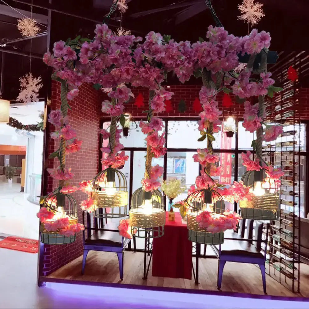 Pink artificial flower garlands hang from ceiling structure with decorbites™ industrial metal black island pendant light fixture height includes five bulb cage lanterns emitting warm light