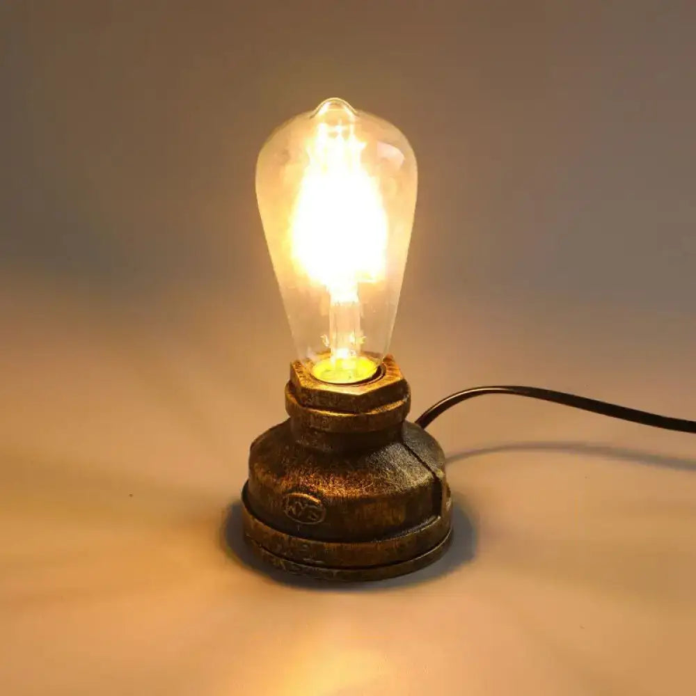 A warm glowing edison led incandescent night light table lamp with rustic brass pipe base and wrought iron accent bronze