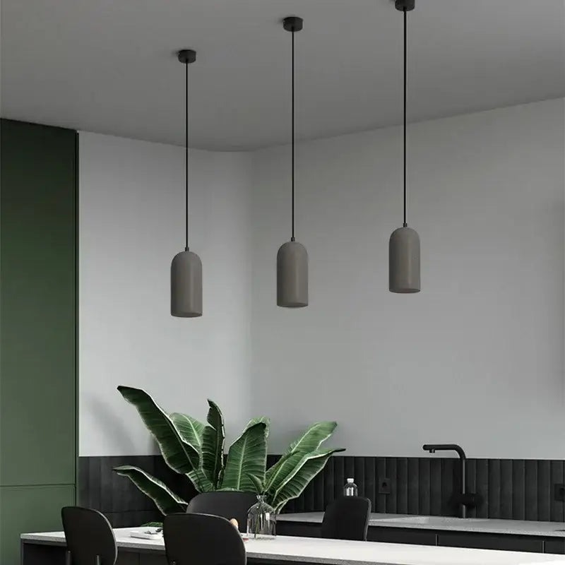 Three modern matte gray cylindrical shades with black cords hang from the ceiling in the decorbites led cement chandelier