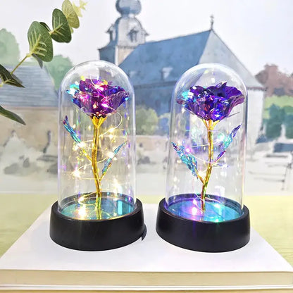 Two iridescent purple DecorBites™ eternal rose lights with golden stems and blue leaves under glass domes for weddings