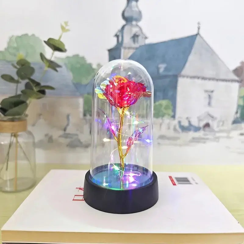 A glowing red eternal rose light with a golden stem in a glass dome illuminated by colorful led lights for decor