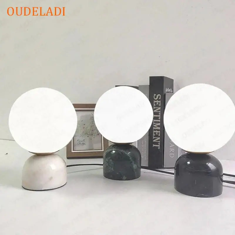 Three decorbites led glass ball table lamps with spherical white glass shades and marble bases in cream dark green and black