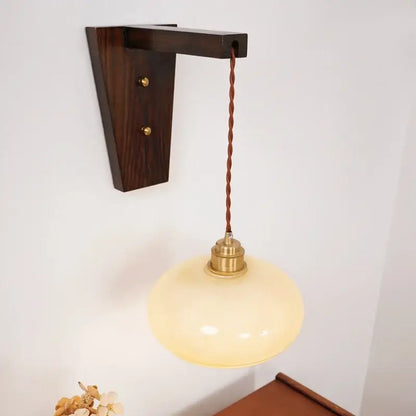 Warm cream-colored led glass sconce wall lamp by decorbites with brass fixture and twisted brown cord on dark wood bracket