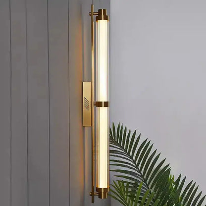 Gold-toned cylindrical DecorBites LED glass wall lamp with frosted glass tube and minimalist metal accents for living room
