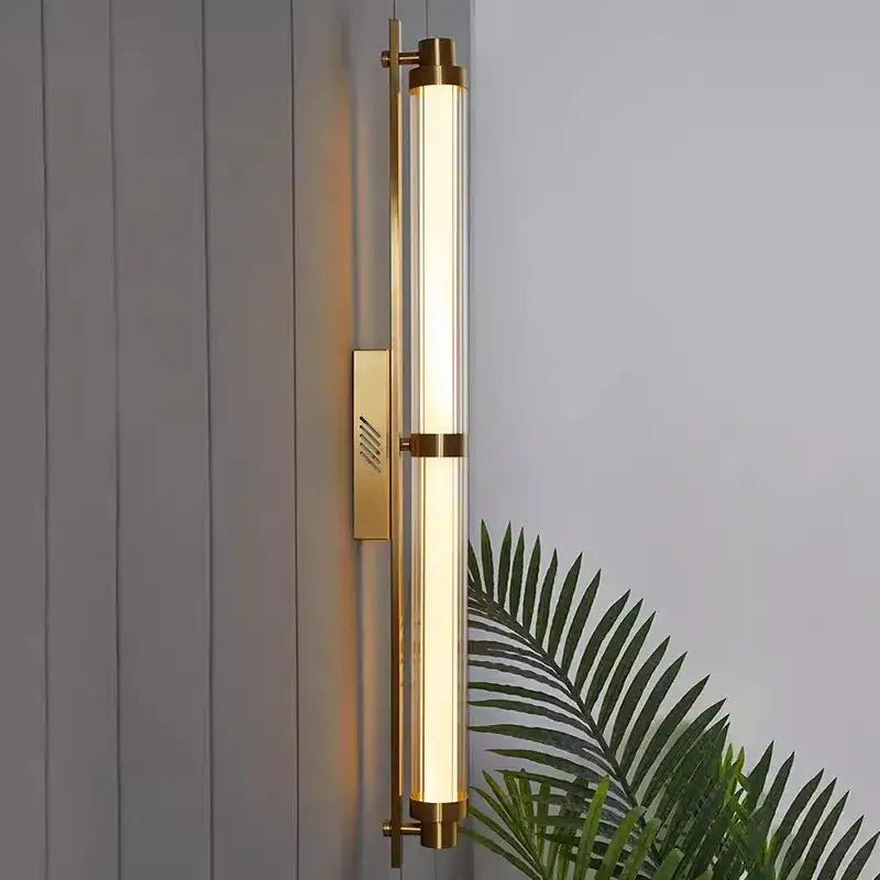 Gold-toned cylindrical DecorBites LED glass wall lamp with frosted glass tube and minimalist metal accents for living room