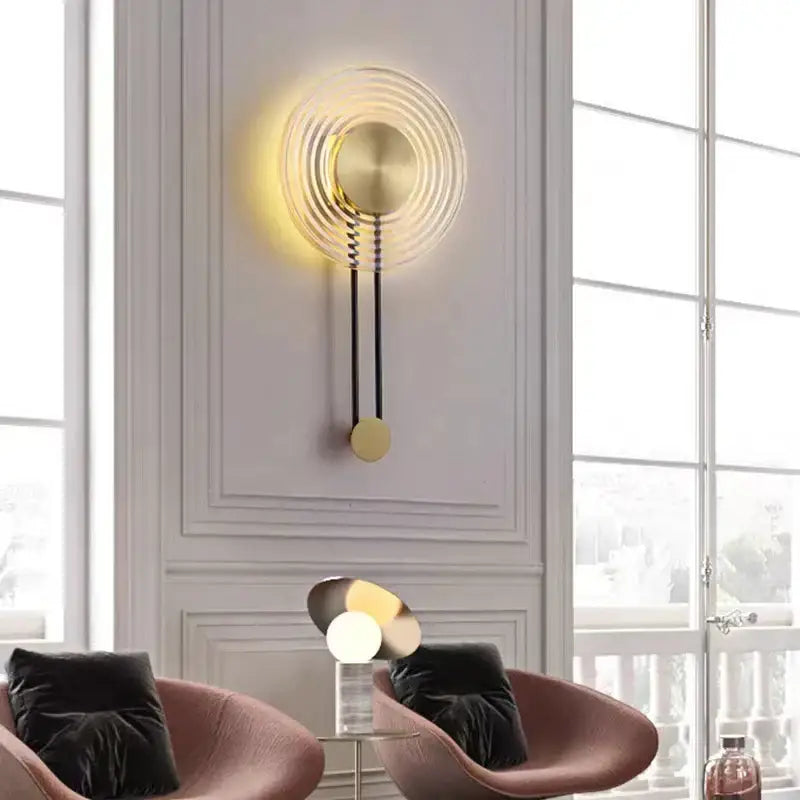 Gold-toned decorbites led glass wall lamp with concentric circular rings and a hanging pendulum-style weight