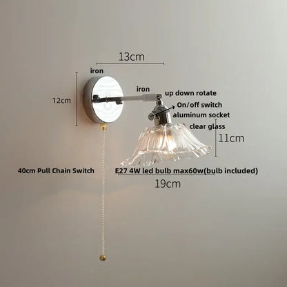 A sleek decorbites led glass wall light with polished iron base and clear flared glass shade for modern bedside use