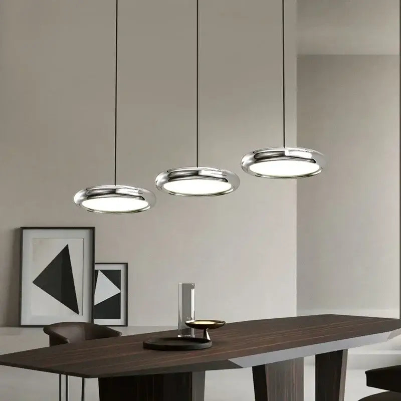 Three polished chrome decorbites led iron pendant lights with circular diffusers in a minimalist dining space