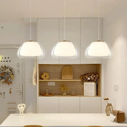 Three modern DecorBites led jelly pendant lights with frosted glass shades and gold fixtures above white countertop